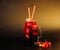 A glass mug of fresh juice with ice and straws on a black background, next to an assortment of ripe berries