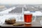 A glass mug of hot black tea and sliced ginger root stand on a wooden surface against a blurry background of a winter city.