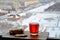 A glass mug of hot black tea and sliced â€‹â€‹ginger root stand on a wooden surface against a blurry background of a winter city.
