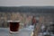 A glass mug with hot black tea stands on the parapet of the roof against the blurred background of the city of Tolyatti.