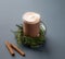 Glass mug of hot chocolate with whipped cream on a stand with pine branches on a gray background with cinnamon stick