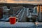 A glass mug with hot tea standing on a snow-covered parapet of the roof against a blurred background of the morning city panorama.