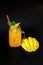 A glass mug of yellow nectar with ice and a diced ripe mango next to it on a black background