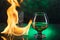 Glass o whisky with ice and wineglass of cognac and fire flames on green bokeh background