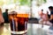 Glass ofdark spanish vermouth drink with slice of orange, a popular aperitif, on outdoor bar table with people during summer day