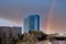 Glass office buildings and apartments along a side a set of railroad tracks with blue sky and powerful clouds and a rainbow