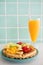 A glass of orange juice with a waffle with fresh fruits