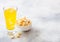 Glass of orange soda drink with ice cubes and white bowl of popcorn snack on stone kitchen table background