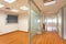 Glass partition enclosing empty office room from corridor with window at end. Outdated design of office corridor and