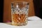 A glass patterned glass with whiskey or cognac stands on the table on a white background the glass is illuminated side