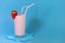 Glass of pink strawberry milkshake or cocktail decorated berry on blue background