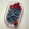 A glass plate holds raspberries, a strawberry, and blueberries