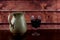 Glass of Red Wine and Earthenware Wine Jug on a Varnished Wooden Shelf