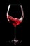 A glass with red wine is isolated on black background. Rose wine splashing in glassware.