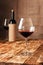 A glass of red wine next to a bottle in burlap on a wooden table in the cellar of the winery
