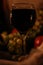 Glass of red wine with reflection of two candles flames on it close up and fruits: grapes, apple on sackcloth background