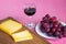 Glass of red wine, sliced yellow cheese Edam on brown wooden cutting board and sweet red grapes on white plate. Still life on a