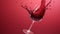 Glass of red wine spilling on red background