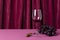 Glass of red wine for tasting, grape and handle corckscrew on the pink table against folds of red curtian.Empty space