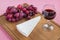 Glass of red wine, triangular piece of Brie cheese and red sweet grapes on brown wooden cutting board. Soft cheese covered with
