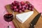 Glass of red wine and a triangular piece of Brie cheese, red sweet grapes, chef knife on a brown wooden cutting board. Soft cheese