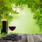 Glass of red wine on wooden background with green grapevine