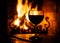 Glass of red wine on the wooden table with burning fire on the background. Evening relax on cozy place. Dark medieval