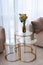 Glass round bedside table with gold with a vase of flowers in a modern beige interior. Interior Design. Soft selective focus,