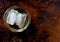 Glass of scotch with three ice cubes, left of center, on a brown background