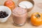 Glass of smoothie of persimmon and blackcurrant with milk, decorated by ingredients on rustic wooden board