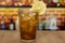 Glass with sparkling cola, ice and lemon on a wooden counter in front of a bar