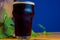 Glass of stout on a wooden table with leaves of hop against the background of barrels