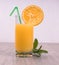 A glass with a straw decorated with an orange slice and mint on a light background