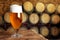 Glass of tasty beer on wooden table in cellar with large barrels, space for text