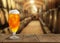 Glass of tasty beer on wooden table in cellar with large barrels, space for text