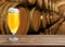 Glass of tasty beer on wooden table in cellar with large barrels, space for text