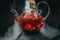 Glass teapot filled with flowers and berries, green tea. Appetizing beautiful drink in orange tones on a black background. Close