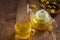 Glass teapot and tea cup with golden dandelion flower tea on the wooden background. Eco friendly organic beverage, healthy life