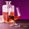 glass textured square bottle and glass goblet with amber alcohol brandy scotch whiskey. violet background. square