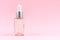 Glass transparent mockup bottle with dropper with cosmetic serum, oil, on pastel pink background.