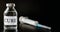 Glass vaccine vial with label Cure on black board, hypodermic syringe near