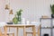 Glass vase with flowers on white wooden table with plate, coffee mugs and jars, real photo with copy space