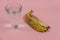 A glass of water and a banana peel on a pink background. A full glass of drinking water. Close-up. Selective focus