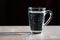 Glass with water on a black background. Bubbles rise up. A glass mug filled with water stands on a wooden table. A cup of water