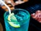 A glass of water with bright green and blue drinks like the Blue Ocean. There are lemon slices on top. The background is the food