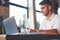 Glass of water in focus. Adult man sits in cafe at daytime and using the laptop for the remote work