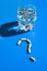 Glass of water and pills in shape of question mark on blue background. Hard light and shadows. Vitamins and prebiotics, probiotics
