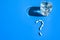 Glass of water and pills in shape of question mark on blue background. Hard light and shadows. Vitamins and prebiotics, probiotics