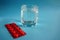 Glass of water with red plate of pills on blue background