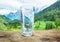 Glass of water on the stone. Blurred snow mountains tops and green forests at the background